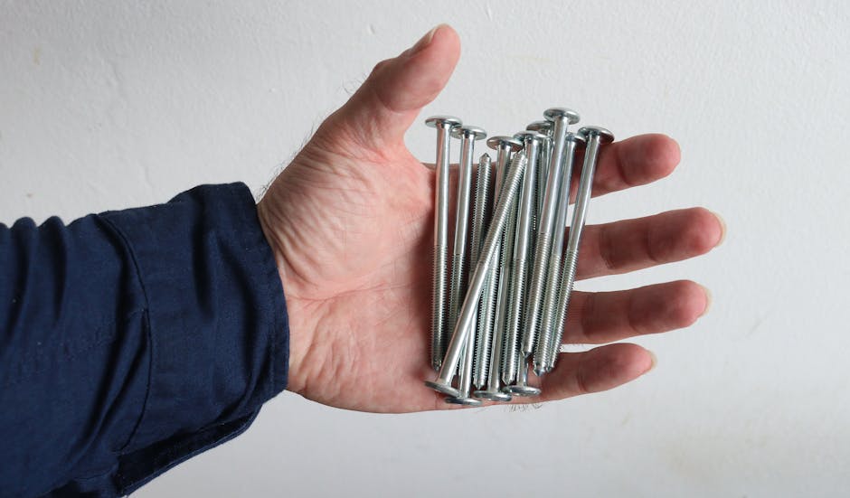 A hand holds several metal screws against a white background.