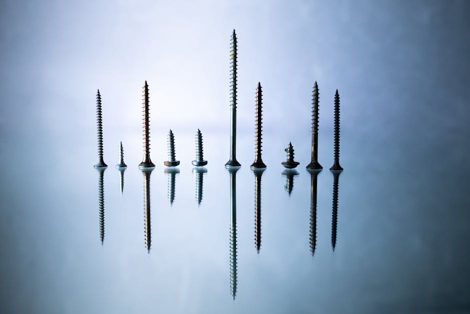 Artistic shot of various screws standing on a reflective surface against a blue-gray background.