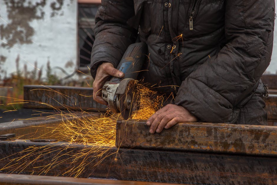 Close-up of a worker using a grinder on metal beams, with sparks flying.