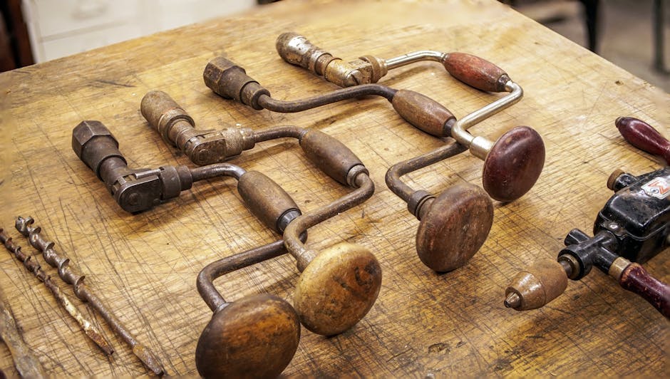 Collection of vintage hand drills with wooden handles on a rustic workbench.