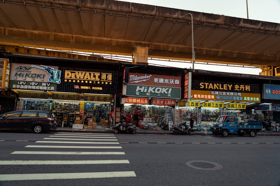Urban street scene showing tool shops under an overpass in a lively city environment.