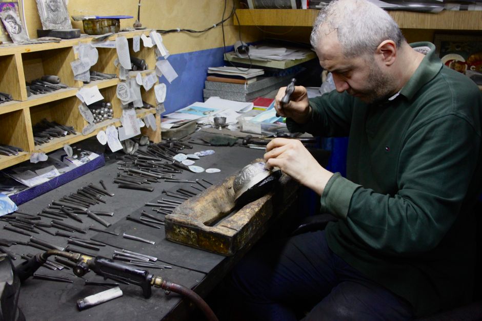 A craftsman focuses on precision engraving in a cluttered workshop.