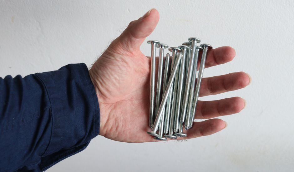 A hand holds several metal screws against a white background.