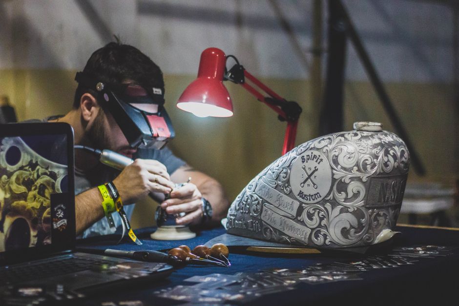 A skilled artisan works on intricate metal engraving under focused lighting in a workshop.