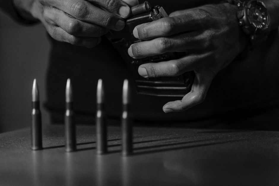 Close-up black and white image of hands loading bullets into a magazine.