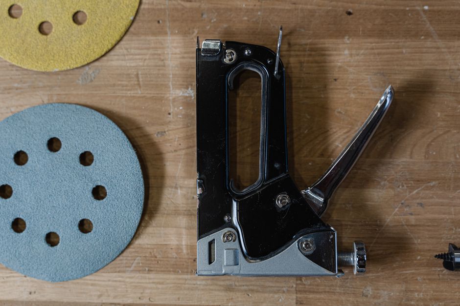 Detailed view of a staple gun alongside sanding discs on a wooden table.