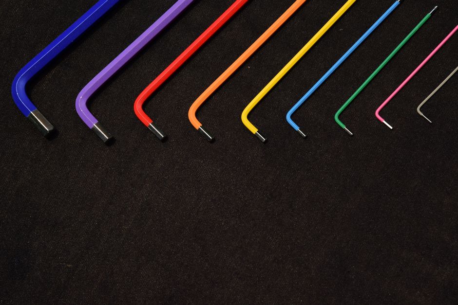 Vibrant L-shaped Allen wrenches in various colors aligned on a textured surface.