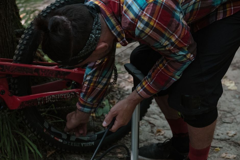 A cyclist inflates a mountain bike tire in a forest setting, ready for a downhill adventure.