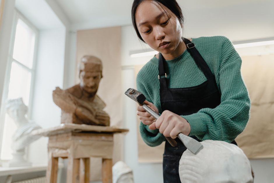 A dedicated sculptor works with a chisel in an art studio, carving intricate details into a statue.