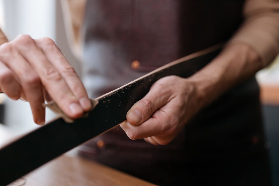 Close-up of hands sanding a wooden strip with sandpaper in a workshop setting.