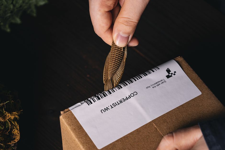 Close-up of hands using a novelty feather tool to open a parcel box indoors.