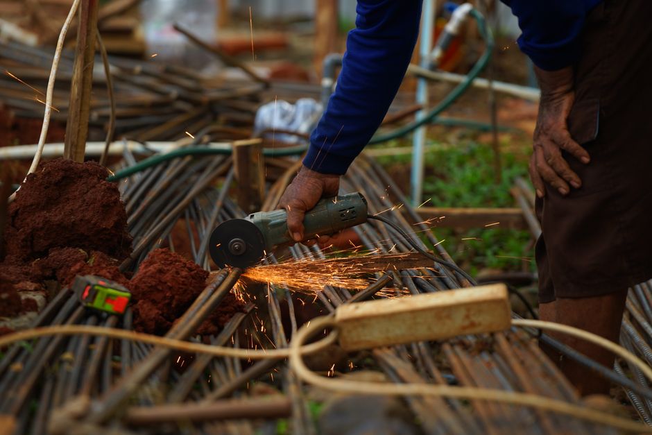 Construction worker cutting steel rebar with an angle grinder, sparks flying in an industrial site