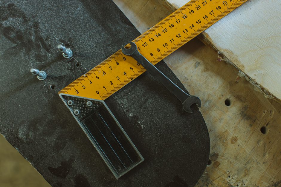 Detailed view of skateboard assembly tools including ruler and wrench on a wooden workbench.