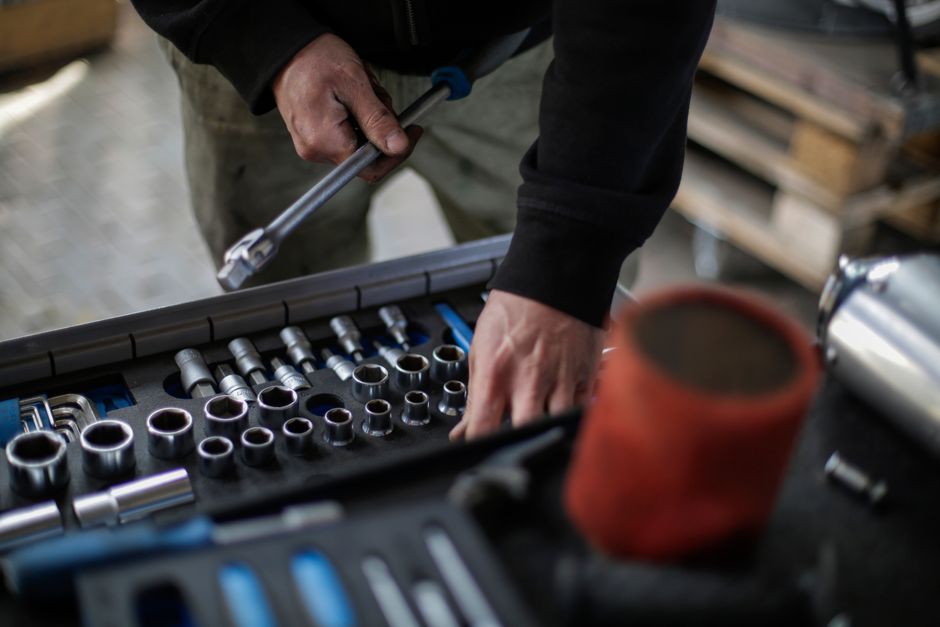 From above view of crop unrecognizable mechanic in workwear choosing metal sockets for ratchet while repairing vehicle in modern workshop