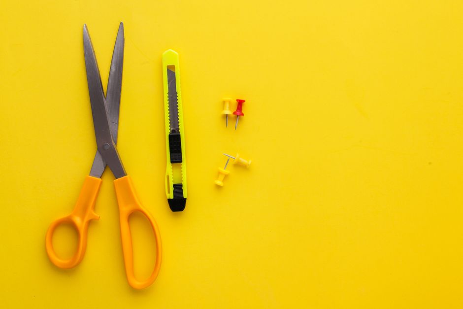 Scissors, utility knife, and push pins on a vivid yellow background.