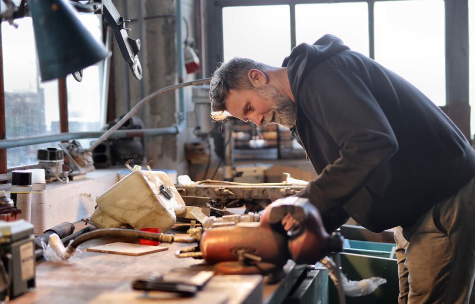 Side view of brutal male worker in casual wear standing at workbench and fixing metal details while using tools and working in workshop