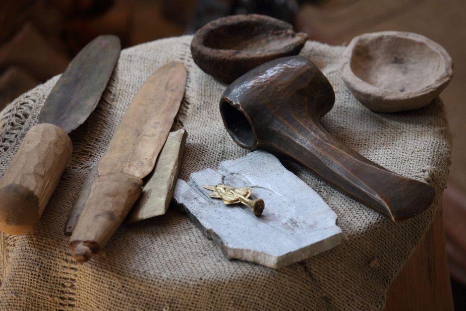 A collection of ancient tools and artifacts displayed on a burlap covered surface.