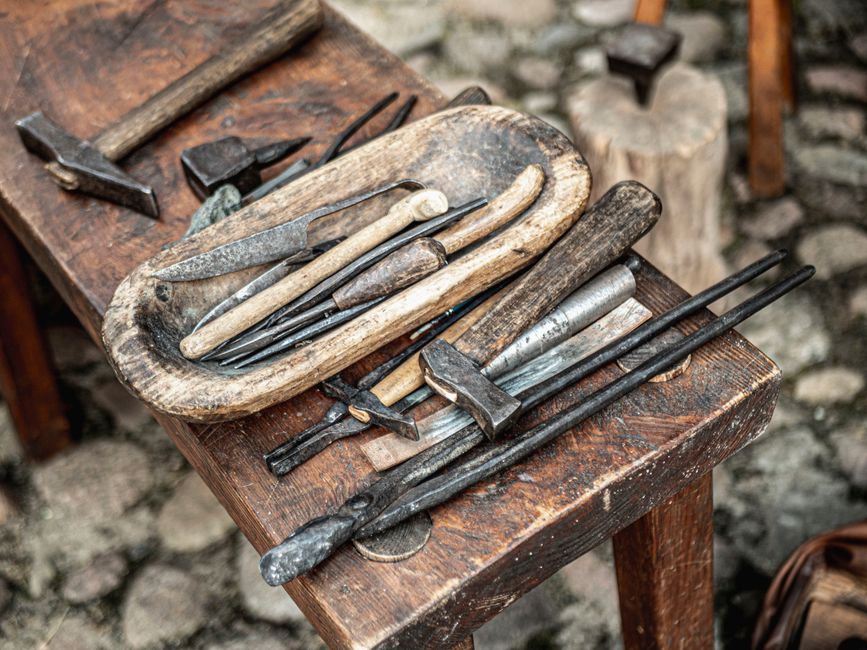 A collection of vintage blacksmith tools displayed on a wooden table outdoors.