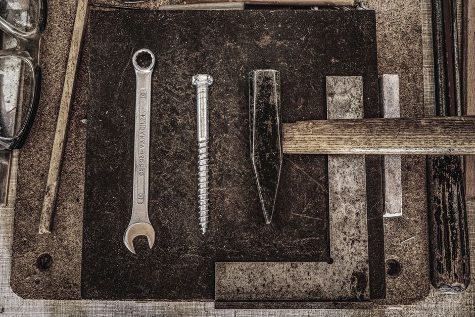 A collection of vintage workshop tools including a wrench, nail, and hammer displayed on a wooden table.