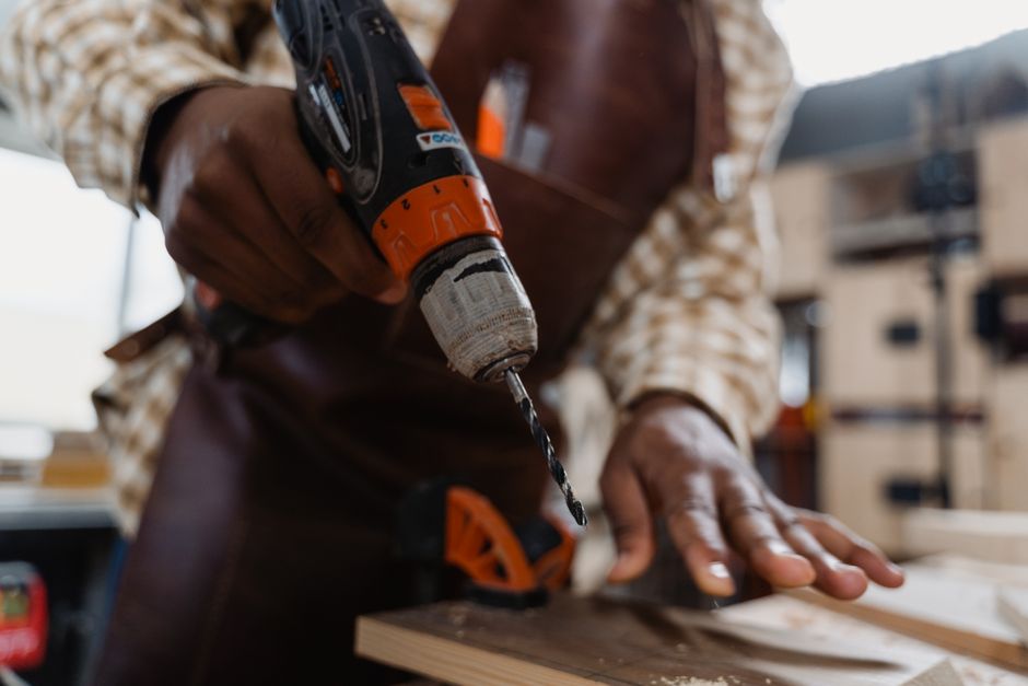 A craftsman skillfully uses a power drill on a wooden plank in a workshop setting.