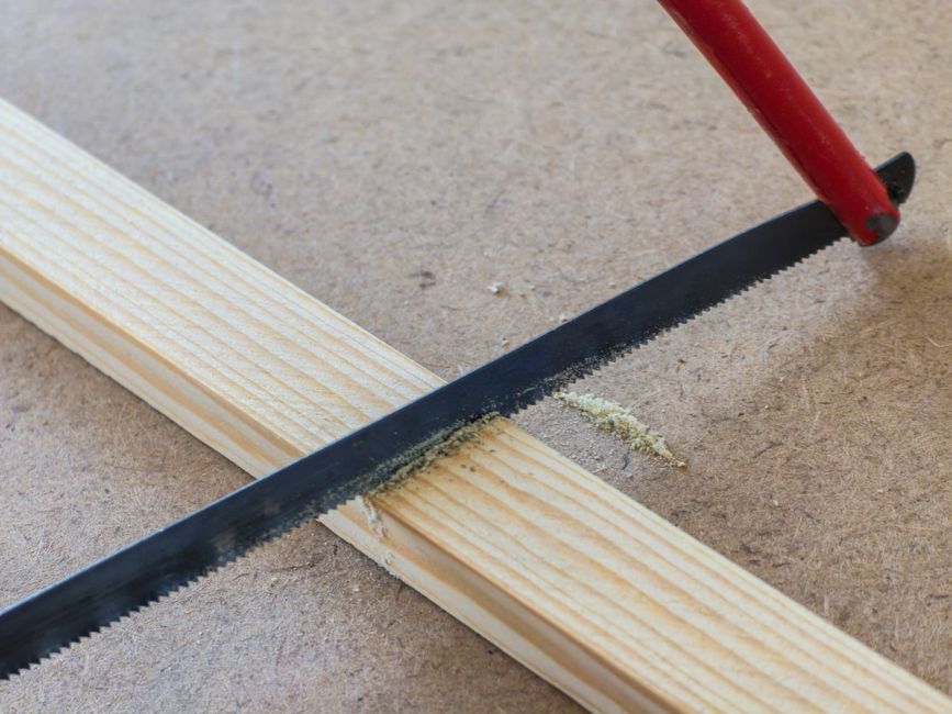 A detailed view of a hand saw cutting through a wooden plank on a workshop bench.