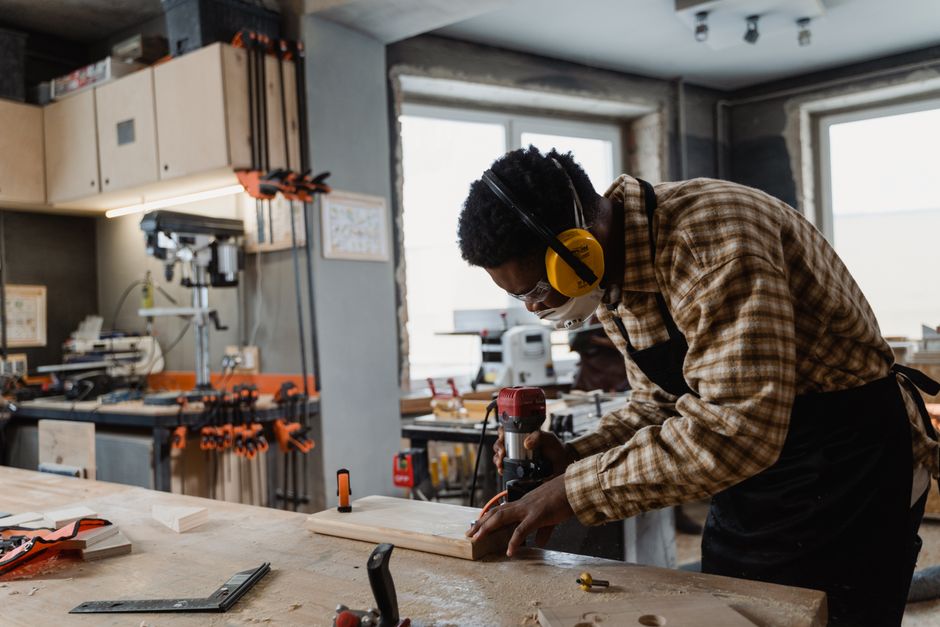 A focused craftsman working intently with woodworking tools and equipment in a workshop.
