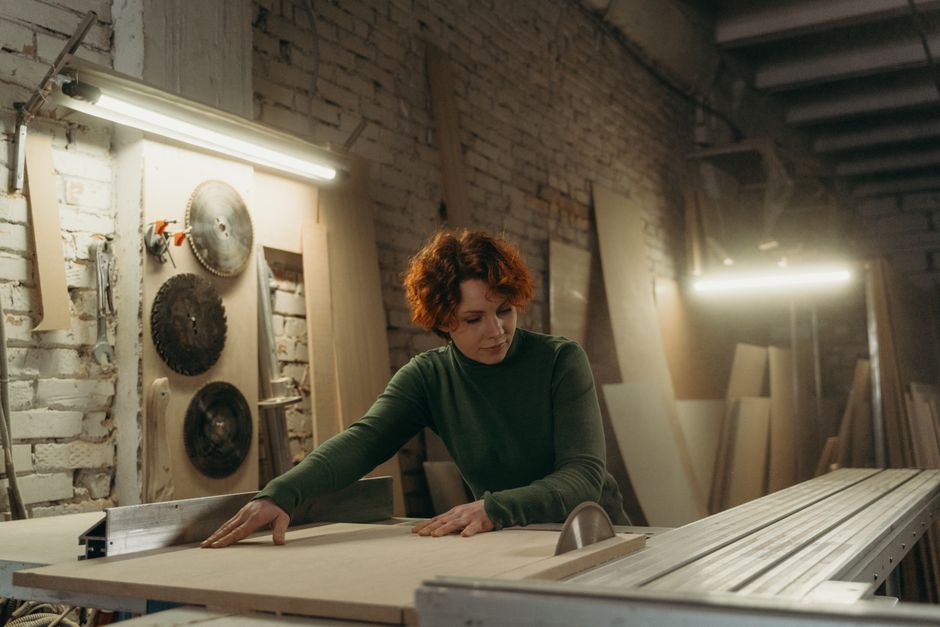 A focused woman working with a circular saw in a woodworking workshop.