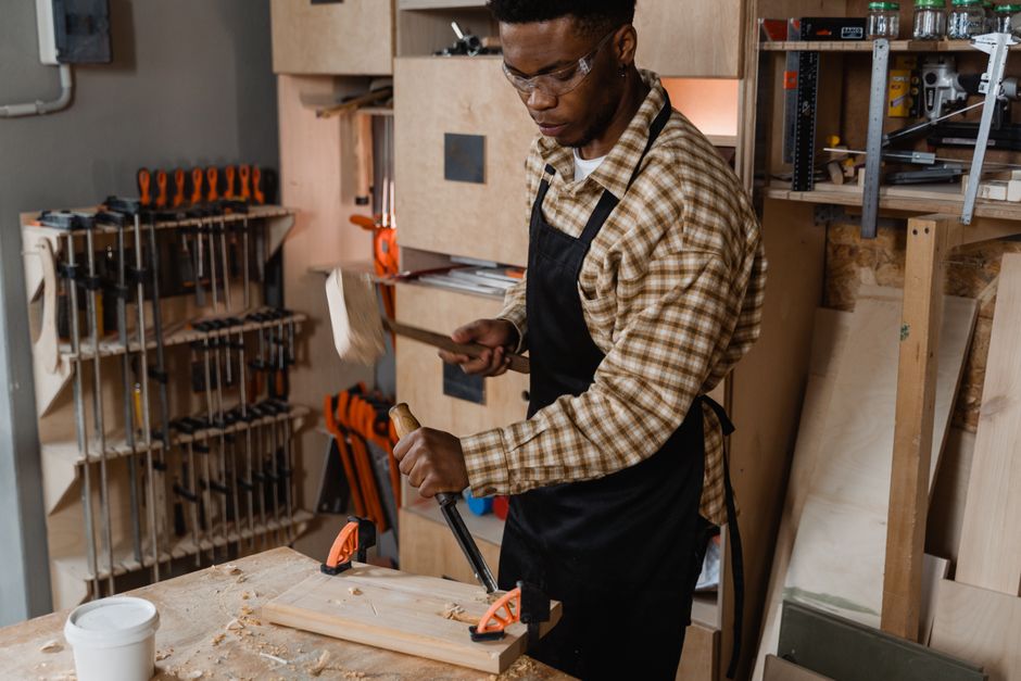 A skilled woodworker carving wood in a workshop environment, surrounded by tools and materials.