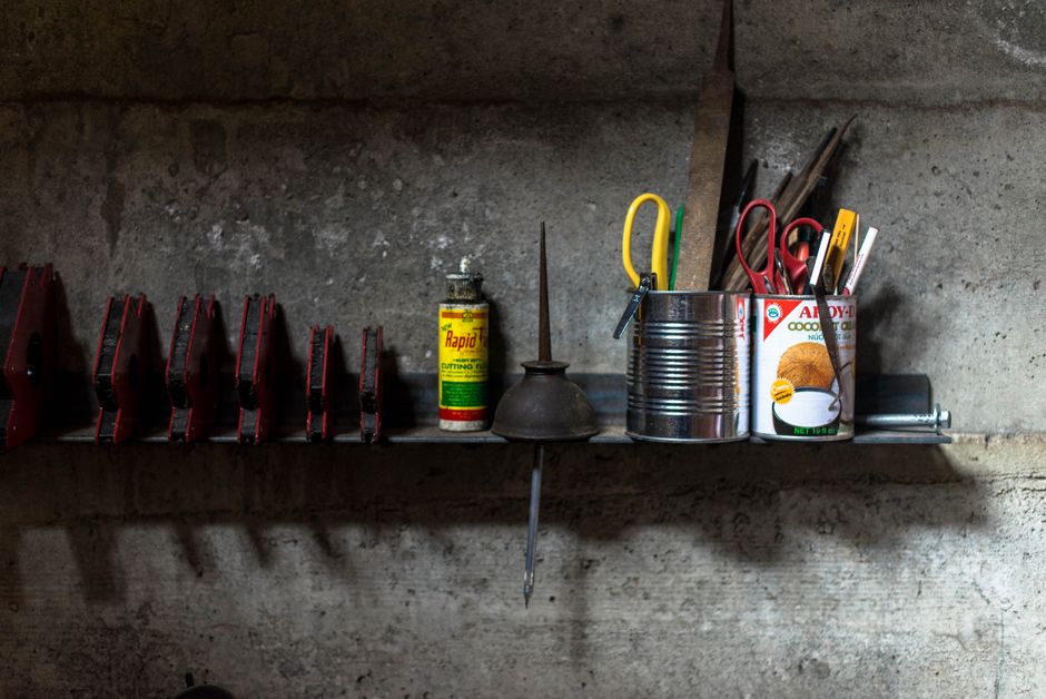 A well-organized workshop shelf with various tools and cans against a concrete wall.