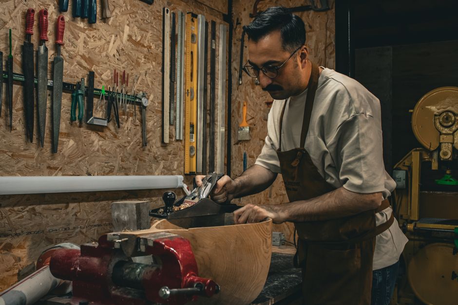 Carpenter using hand tools to shape wood in a workshop environment.