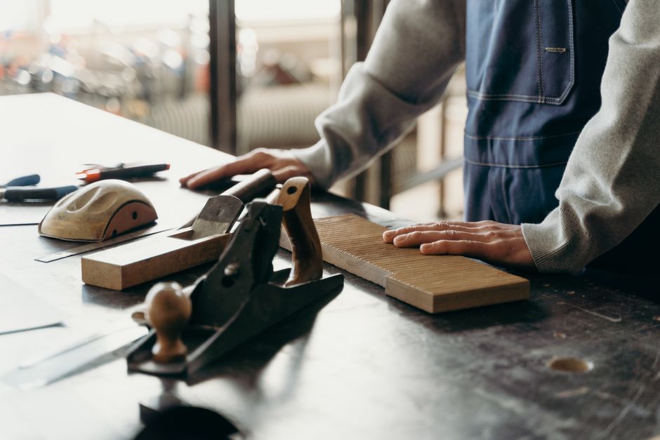 Carpenter working with tools and wood on a table in an industrial workshop.
