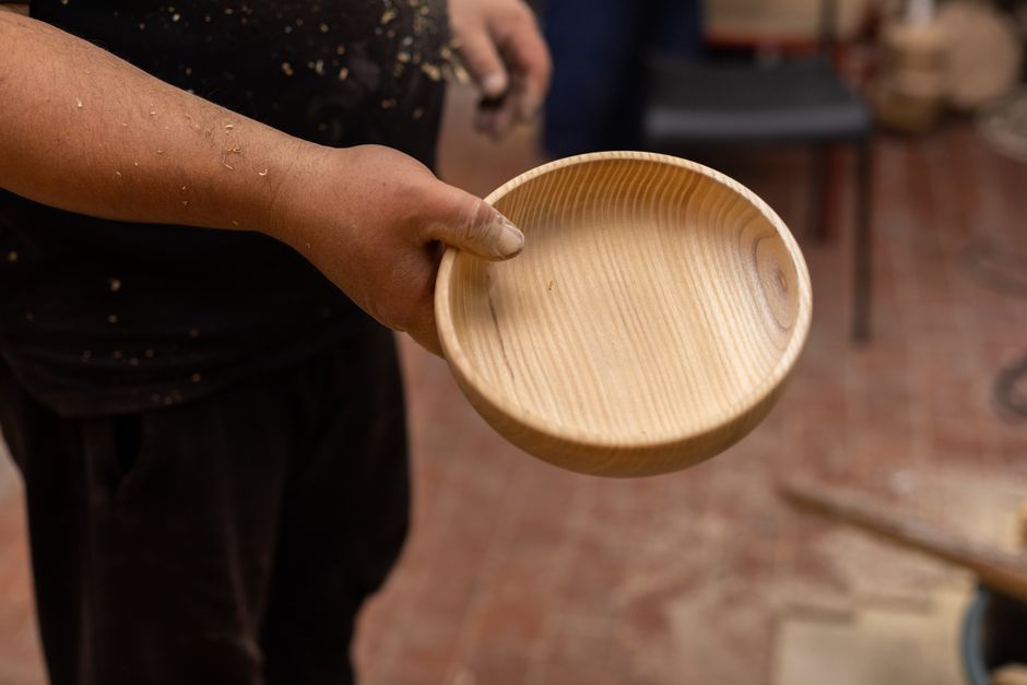 Close-up of a craftsman's hand holding a handmade wooden bowl in a workshop setting.