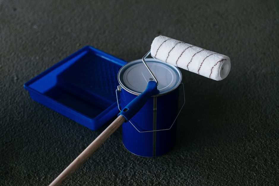 Close-up of a paint can, roller, and tray on a textured floor, perfect for DIY projects.