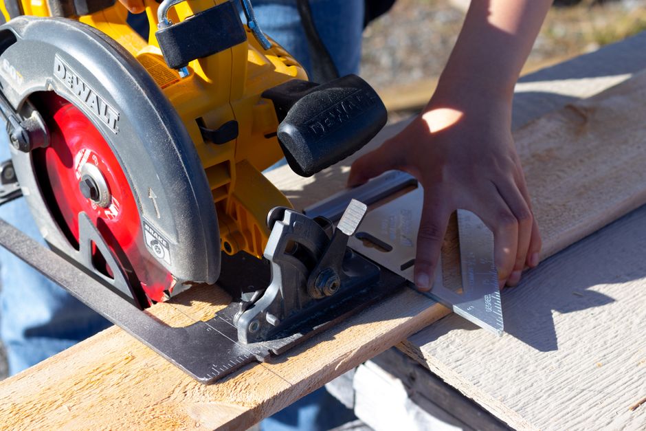 Close-up of a woman using a circular saw and speed square for woodworking outdoors.