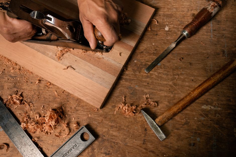 Close-up of hands using a planer on wood with tools and shavings around.