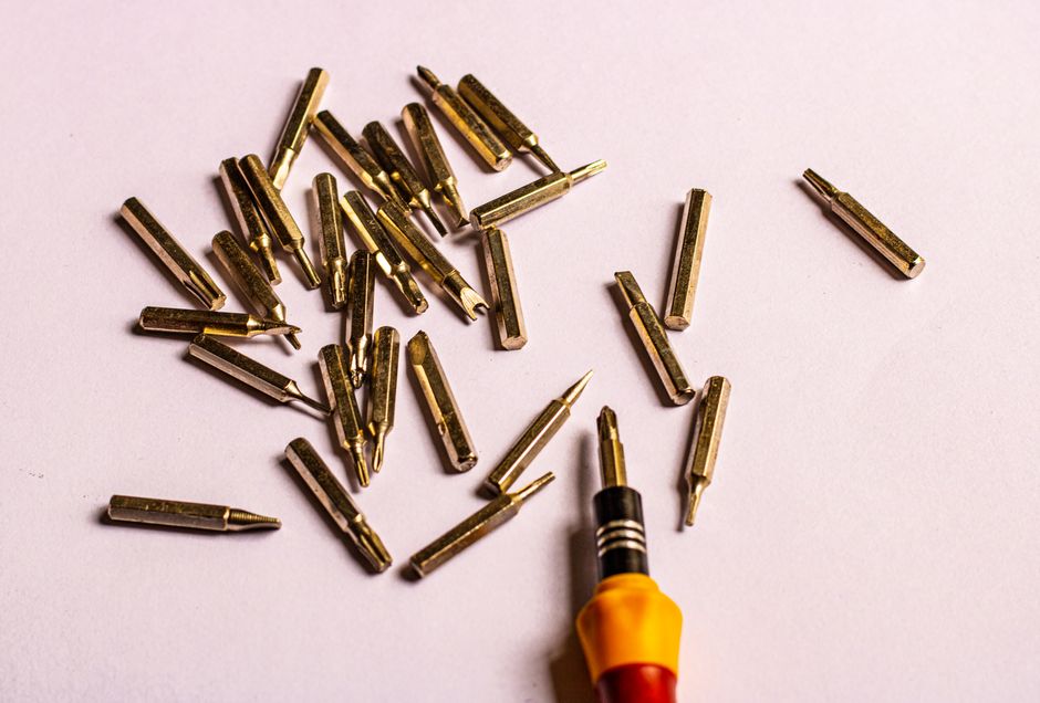 Close-up of various golden screwdriver bits with a handle on a white surface.