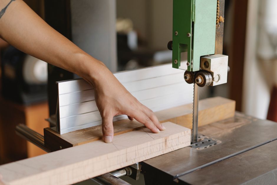 Crop anonymous artisan cutting wooden plank using electric equipment with sharp blade on table