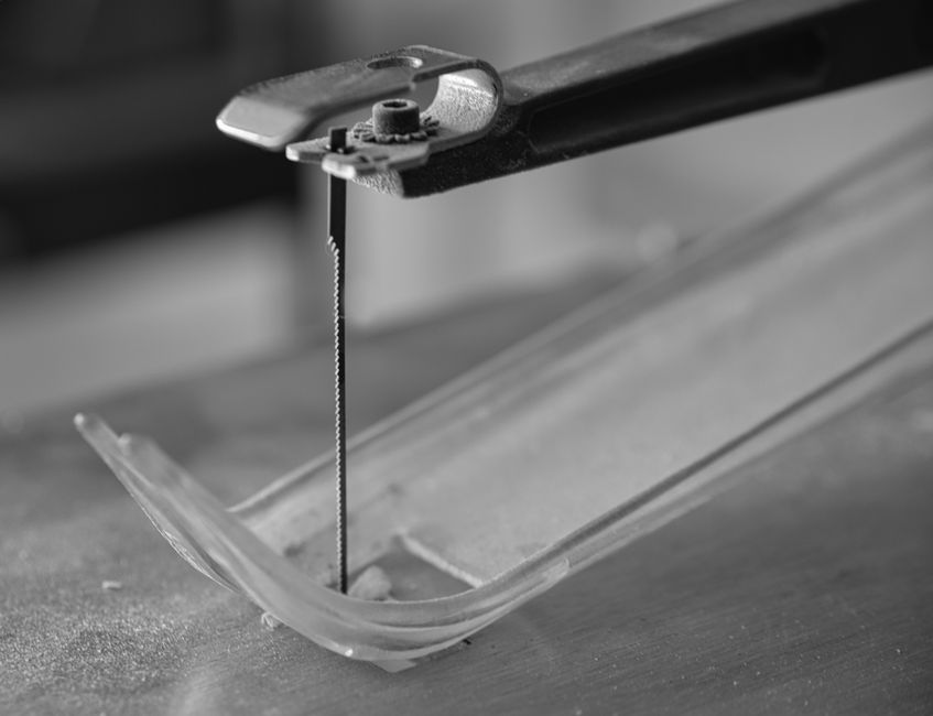 Detailed black and white image of a scroll saw blade positioned for cutting plastic.