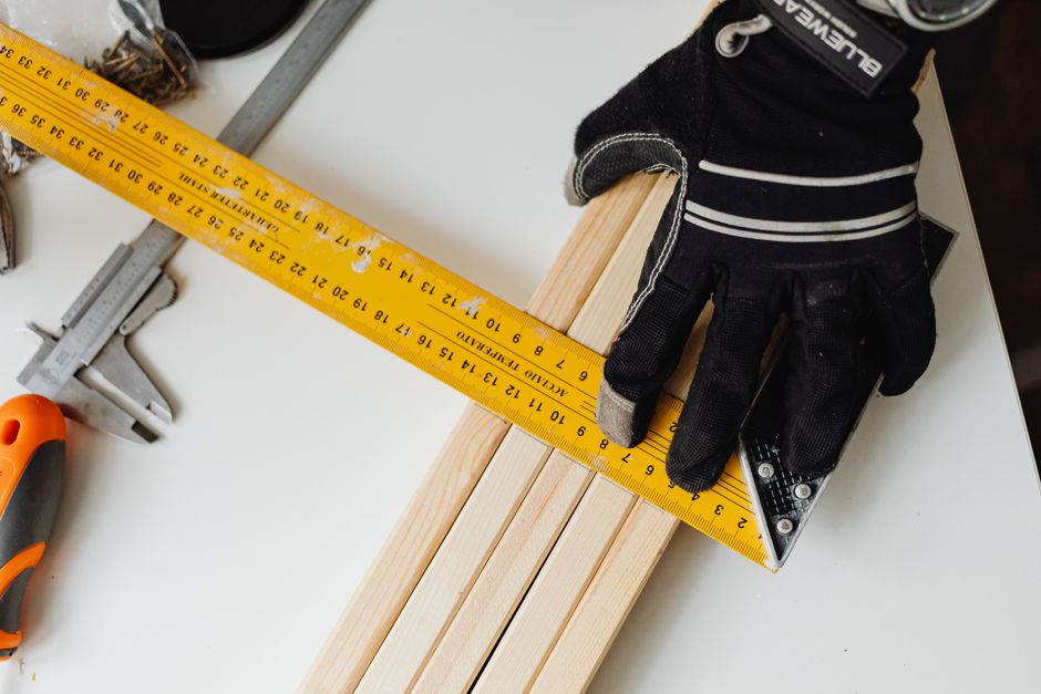 Detailed image of a gloved hand using measuring tools on wood, showcasing precision in craftsmanship.