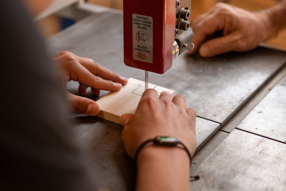 Detailed view of hands operating a band saw, highlighting precision woodworking skills.