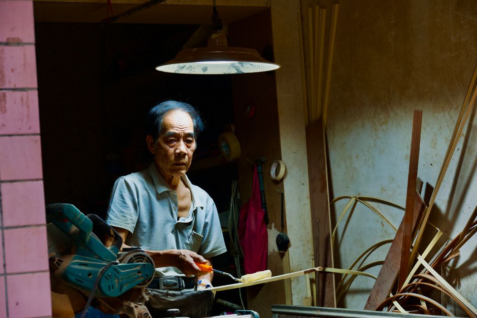 Elderly craftsman meticulously working in a dimly lit workshop, surrounded by tools and materials.