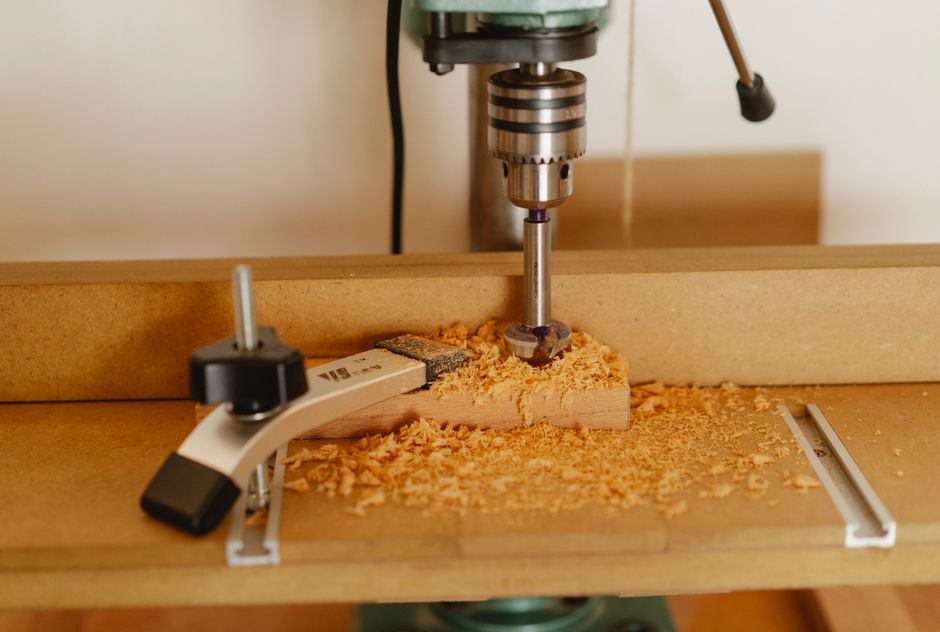 Electric drill press making hole in timber plank fixed with carpenter vice on workshop table