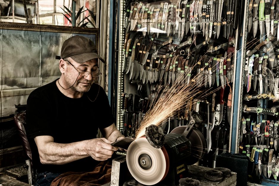Experienced craftsman skillfully sharpens knives in a bustling workshop, surrounded by tools.