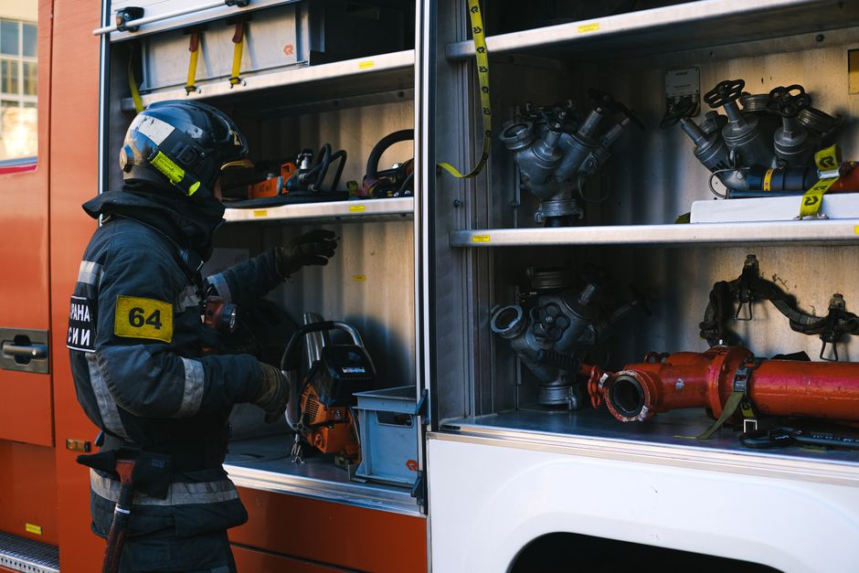 Firefighter arranging equipment and tools in a fire engine's compartment.