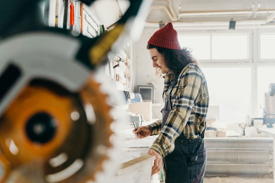 Focused carpenter measuring wood in a well-lit workshop, utilizing a miter saw.