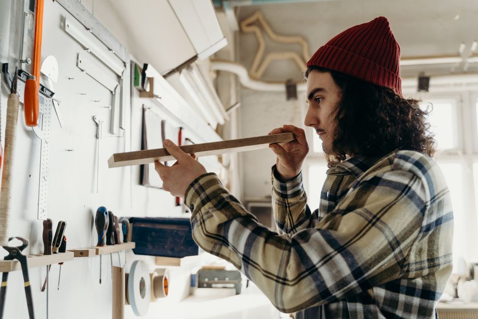Focused young carpenter measuring a wooden plank in a workshop environment. Tools and natural light provide a creative ambiance.