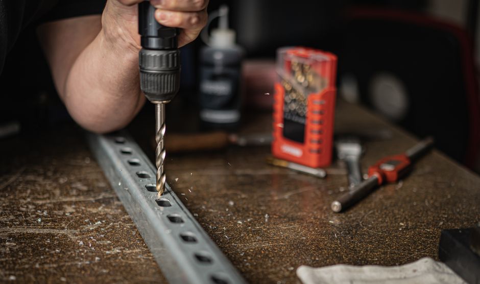 Hand holding a drill, creating holes in metal indoors, emphasizing industrial work.