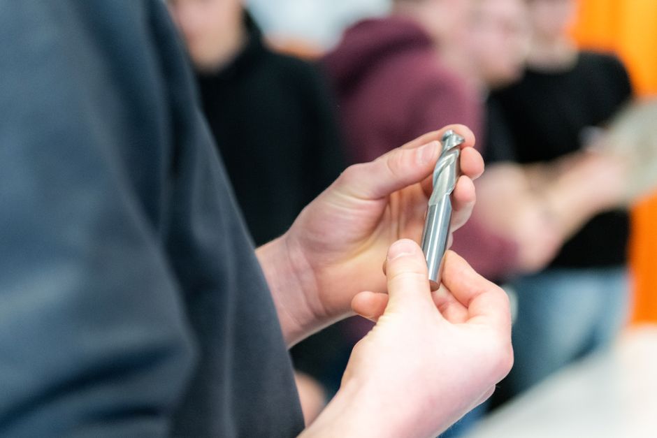 Hands carefully examining a metal drill bit during a workshop session.