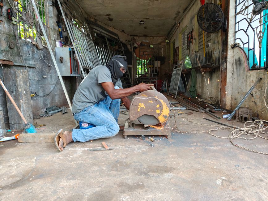 Man in workshop using a metal cutting saw, surrounded by tools and equipment. Sparks flying.