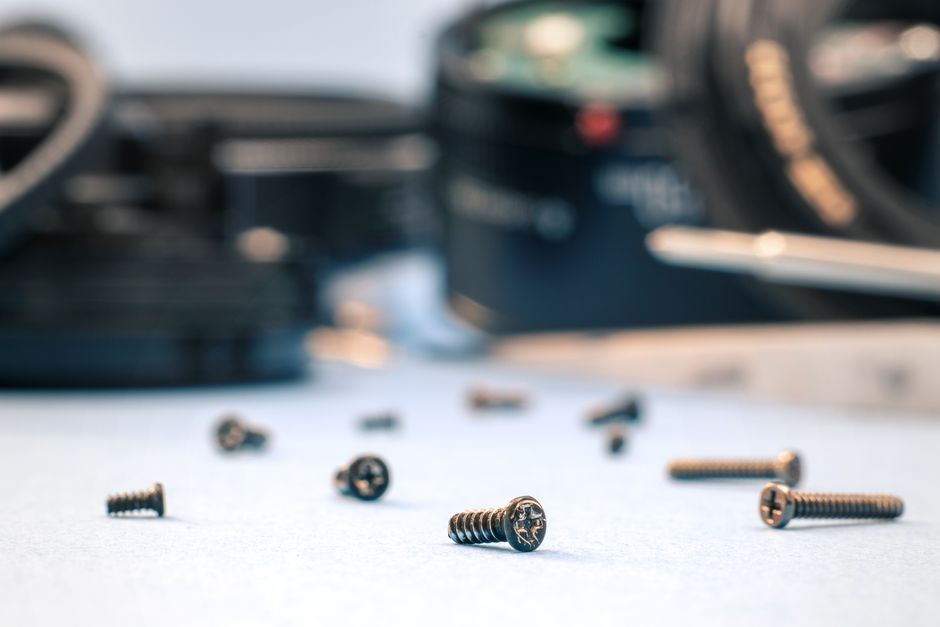 Scattered screws on a white surface with blurred tools, ideal for repair themes.